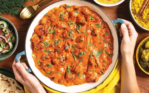 Pyszny **butter chicken przepis oryginalny** w kremowym sosie, podany z ryżem, sałatką i chlebkiem naan.