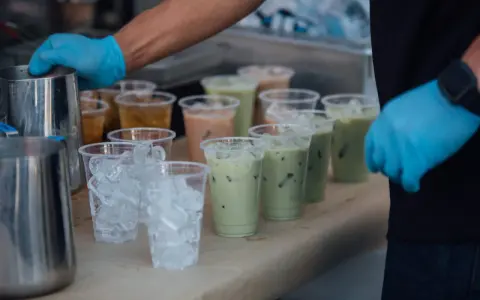 Przygotowanie do zrobienia kulek do bubble tea: ręce w niebieskich rękawiczkach, dzbanki, kubki z lodem i gotowe napoje.