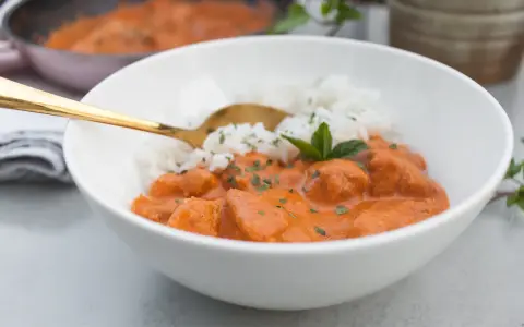 Aksamitny butter chicken masala z ryżem, udekorowany miętą. Złota łyżka zanurzona w daniu.