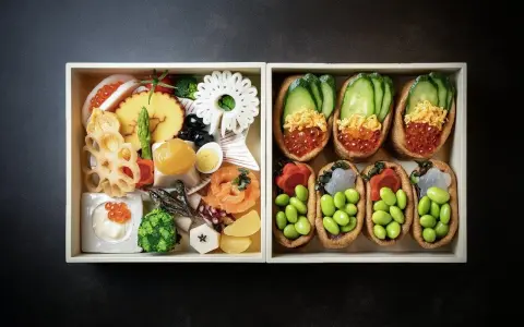 Dwa pudełka z japońskimi przysmakami: jedno z różnorodnymi składnikami, drugie z inari sushi na słodko, wypełnione edamame i ikrą.