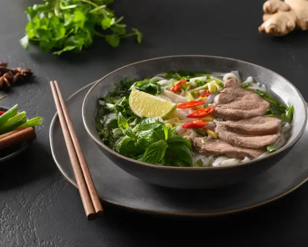 Aromaticzna zupa pho bo z cienko pokrojonym wołowiną, makaronem ryżowym, świeżą miętą, limonką i papryczkami chili.