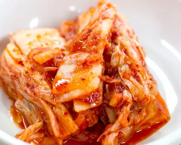 Domowe kimchi w białej misce, z widocznymi liśćmi kapusty i przyprawami.