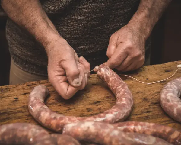 Ręce wiążą kiełbasę sznurkiem. Zastanawiasz się, jak długo wędzić kiełbasę bez parzenia?