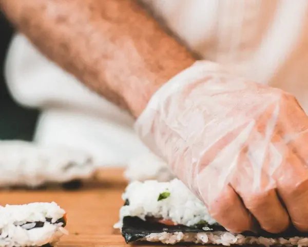 Ręce w rękawiczkach zwijają sushi. Zastanawiasz się, jaka ryba do sushi będzie najlepsza?