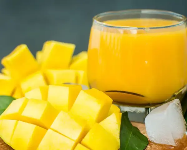 Orzeźwiający mango lassi przepis: pokrojony w kostkę dojrzały mango, szklanka gęstego napoju, kostki lodu i zielone liście.