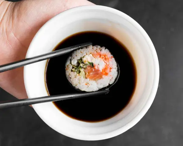 Pałeczki trzymają sushi z łososiem, zanurzając je w miseczce z gęstym słodkim sosem do sushi.