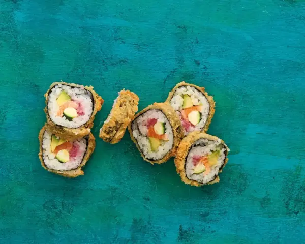 Chrupiące sushi w panko z łososiem, awokado i ogórkiem na turkusowym tle.