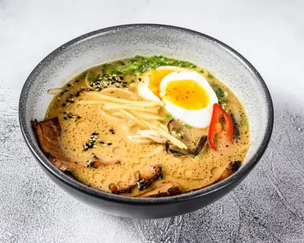 Jak zrobić ramen z zupki chińskiej? Aromatyczny bulion, makaron, jajko na pół, mięso i dodatki w misce.