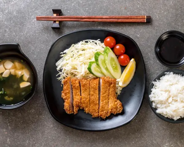 Pyszny schab po japońsku, podany z ryżem, zupą miso, surówką i sosem.