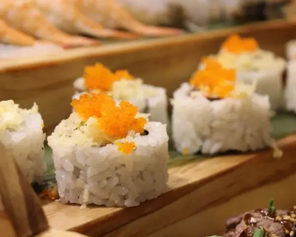Roladki sushi z pomarańczową ikrą i chrupiącą posypką, idealne do słodkiego sosu do sushi.