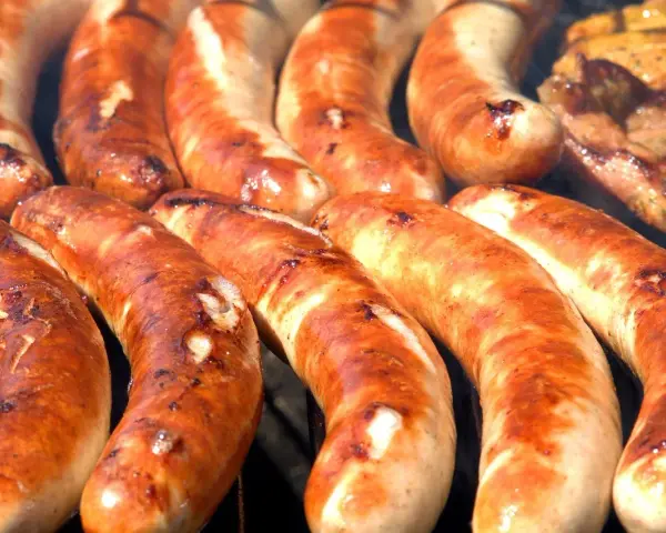 Kilka grubych, rumianych kiełbasek z grilla ułożonych obok siebie.