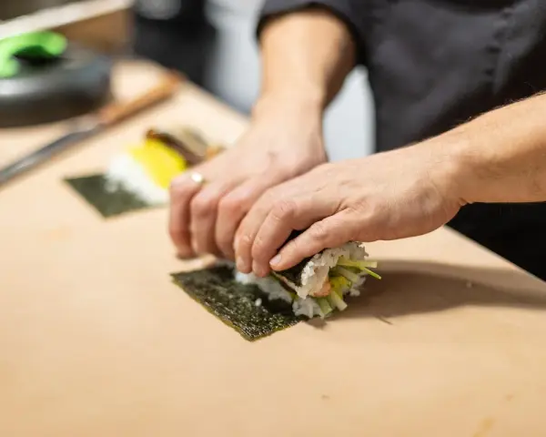 Ręce zwijają sushi na nori. Zastanawiasz się, nori gdzie kupić? W sklepach z azjatycką żywnością lub online.