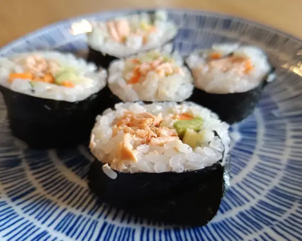 Pięć kawałków sushi z pieczonym łososiem, ryżem i warzywami na niebiesko-białym talerzu.
