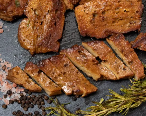 Seitan co to? Pokrojony w plastry, smażony seitan z przyprawami: różową solą, pieprzem i rozmarynem.