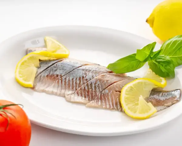 Filety śledzi z cytryną i bazylią na talerzu. Kto nie powinien jeść śledzi? Alergicy i osoby z problemami z cholesterolem.