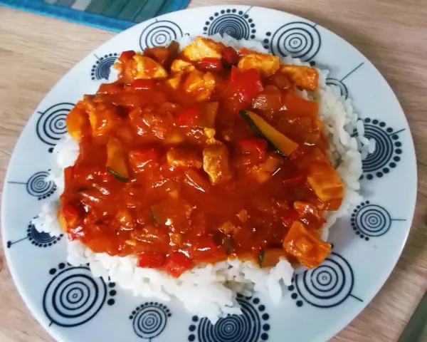 Pyszny, prosty sos do ryżu z kurczakiem i warzywami. Danie podane na talerzu z czarno-białym wzorem.