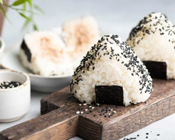Trójkątne japońskie kulki ryżowe onigiri, posypane czarnym sezamem, z kawałkiem nori.