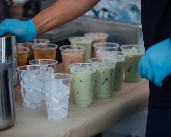Przygotowanie do zrobienia kulek do bubble tea: ręce w niebieskich rękawiczkach, dzbanki, kubki z lodem i gotowe napoje.