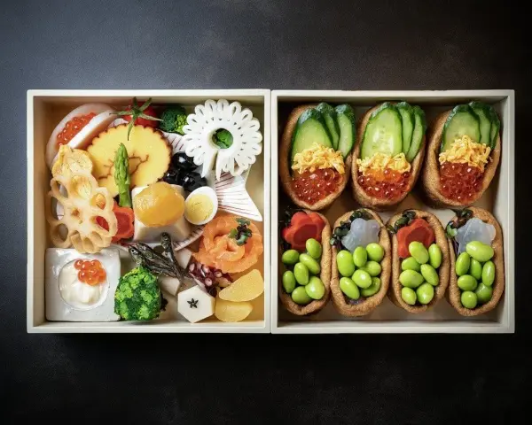 Dwa pudełka z japońskimi przysmakami: jedno z różnorodnymi składnikami, drugie z inari sushi na słodko, wypełnione edamame i ikrą.