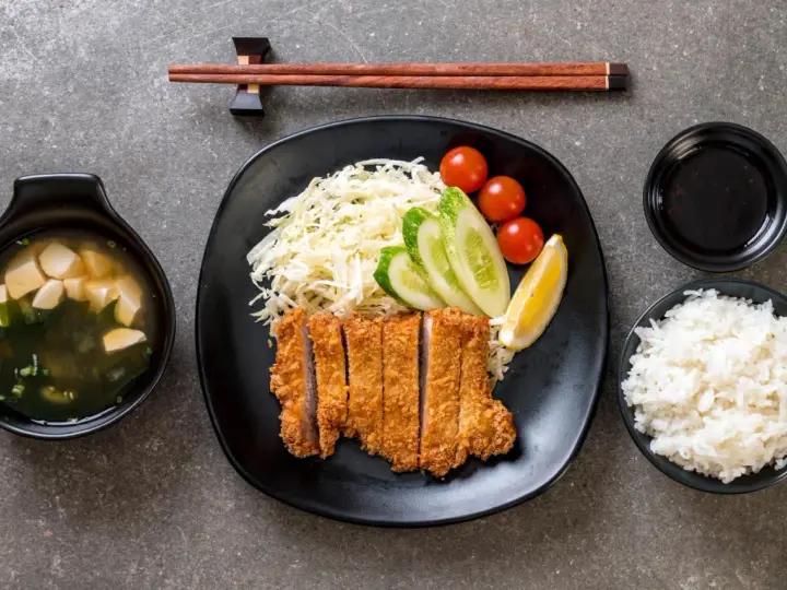 Pyszny schab po japońsku, podany z ryżem, zupą miso, surówką i sosem.