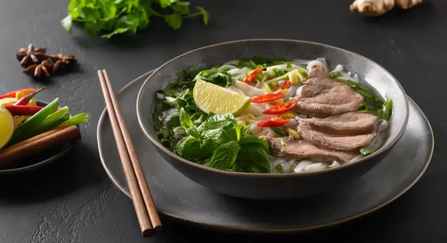 Aromaticzna zupa pho bo z cienko pokrojonym wołowiną, makaronem ryżowym, świeżą miętą, limonką i papryczkami chili.