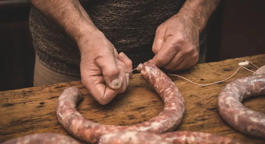 Ręce wiążą kiełbasę sznurkiem. Zastanawiasz się, jak długo wędzić kiełbasę bez parzenia?
