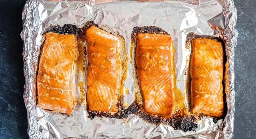 Cztery kawałki łososia pieczone na folii aluminiowej, gotowe do dalszego przygotowania, np. jak przygotować łososia do sushi.