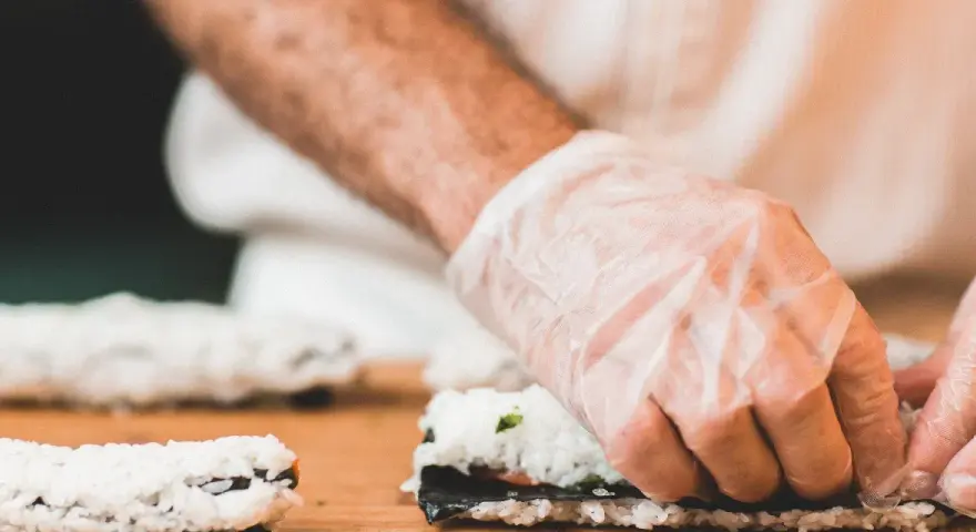 Ręce w rękawiczkach zwijają sushi. Zastanawiasz się, jaka ryba do sushi będzie najlepsza?