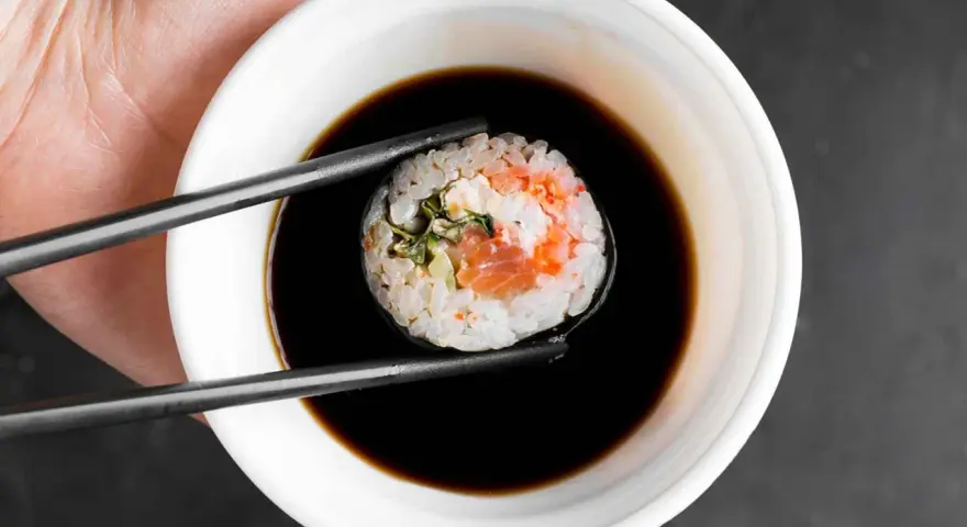 Pałeczki trzymają sushi z łososiem, zanurzając je w miseczce z gęstym słodkim sosem do sushi.