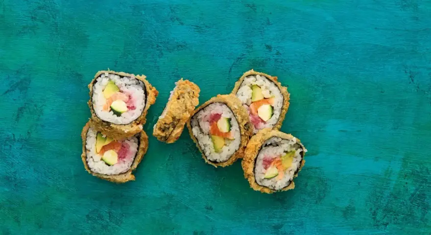 Chrupiące sushi w panko z łososiem, awokado i ogórkiem na turkusowym tle.
