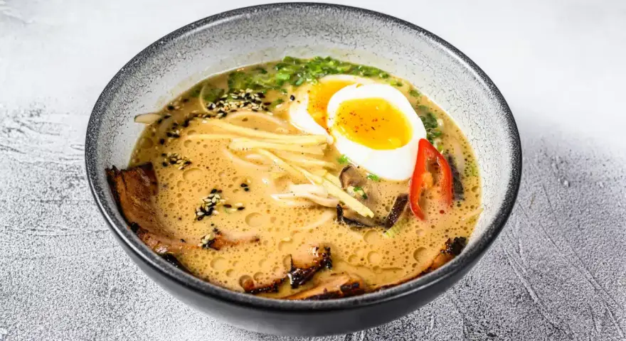 Jak zrobić ramen z zupki chińskiej? Aromatyczny bulion, makaron, jajko na pół, mięso i dodatki w misce.