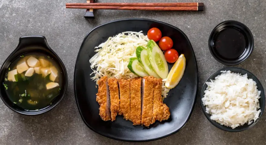 Pyszny schab po japońsku, podany z ryżem, zupą miso, surówką i sosem.