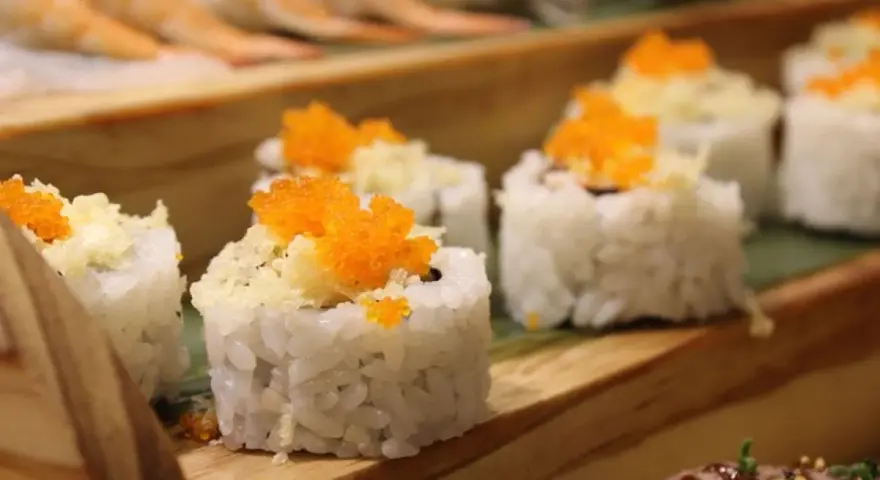 Roladki sushi z pomarańczową ikrą i chrupiącą posypką, idealne do słodkiego sosu do sushi.