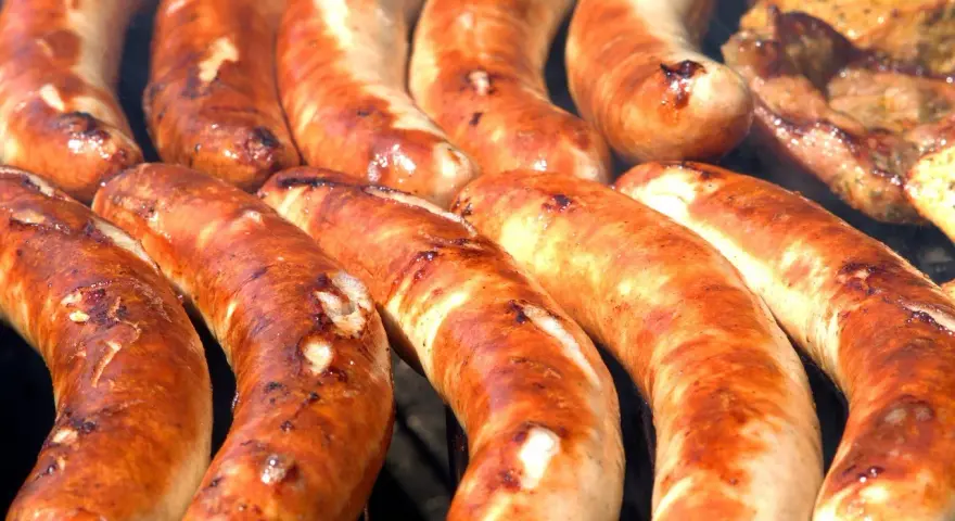 Kilka grubych, rumianych kiełbasek z grilla ułożonych obok siebie.