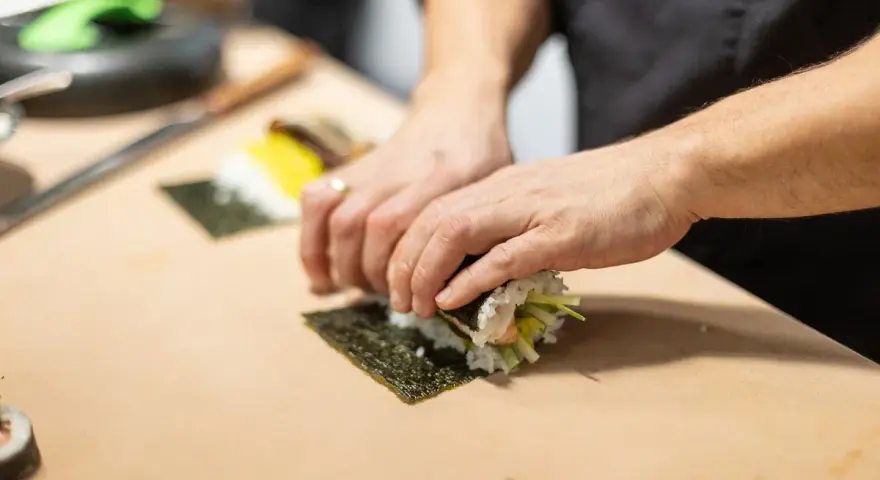 Ręce zwijają sushi na nori. Zastanawiasz się, nori gdzie kupić? W sklepach z azjatycką żywnością lub online.
