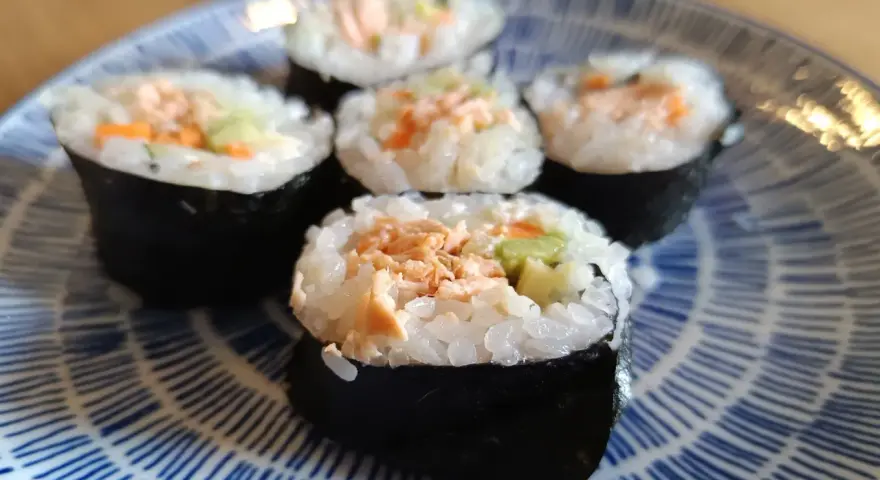 Pięć kawałków sushi z pieczonym łososiem, ryżem i warzywami na niebiesko-białym talerzu.