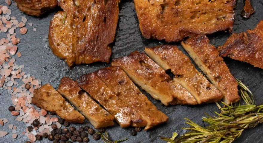 Seitan co to? Pokrojony w plastry, smażony seitan z przyprawami: różową solą, pieprzem i rozmarynem.