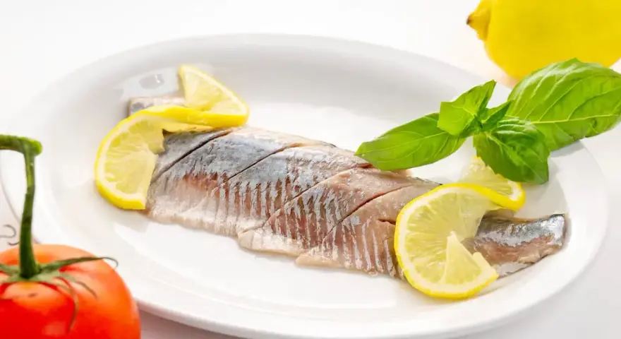 Filety śledzi z cytryną i bazylią na talerzu. Kto nie powinien jeść śledzi? Alergicy i osoby z problemami z cholesterolem.