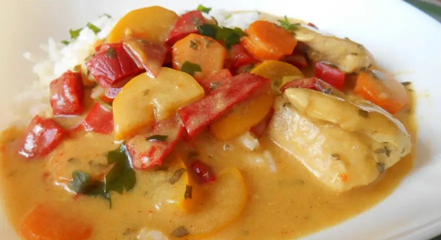 Kurczak curry z warzywami: kawałki kurczaka w kremowym sosie z papryką, marchewką i cukinią, podane z ryżem.