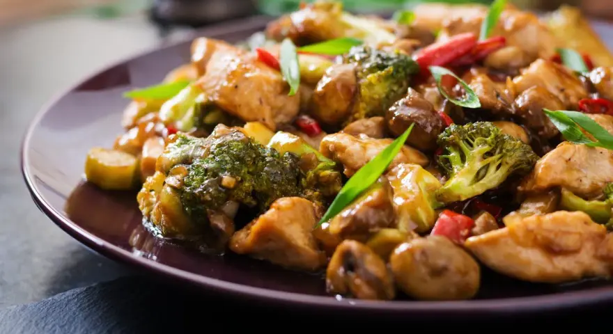 Pyszny stir fry z kurczakiem, brokułami i grzybami w sosie. Danie wygląda apetycznie i jest bogate w kolory.