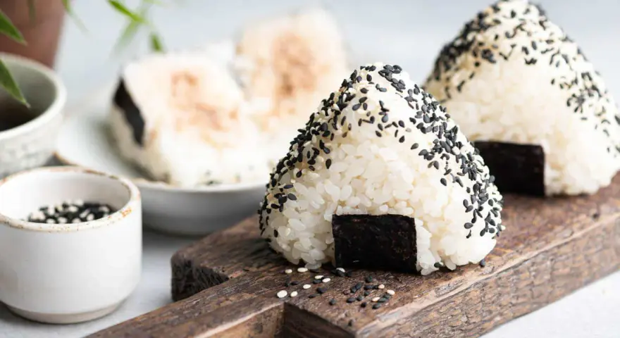 Trójkątne japońskie kulki ryżowe onigiri, posypane czarnym sezamem, z kawałkiem nori.