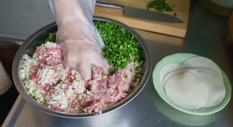 Mieszanie mielonego mięsa, kapusty i szczypiorku do pierożków gyoza. Przepis na pyszne domowe pierożki.