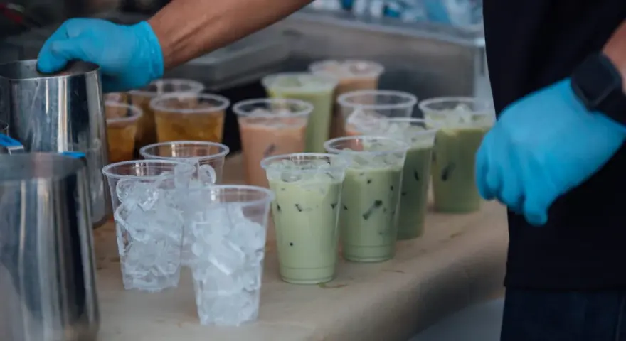 Przygotowanie do zrobienia kulek do bubble tea: ręce w niebieskich rękawiczkach, dzbanki, kubki z lodem i gotowe napoje.
