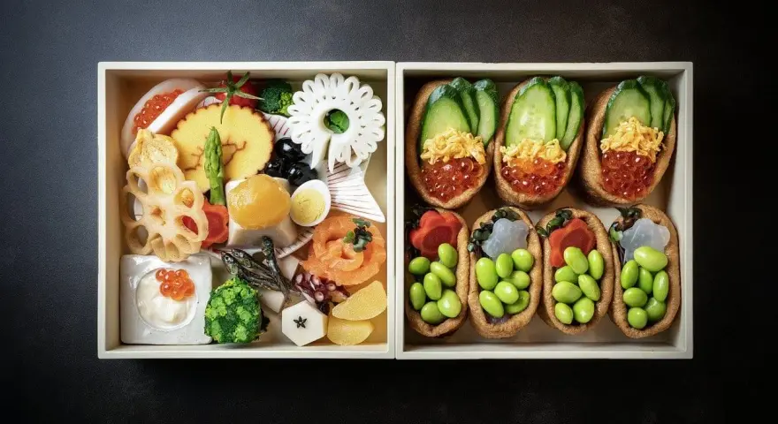 Dwa pudełka z japońskimi przysmakami: jedno z różnorodnymi składnikami, drugie z inari sushi na słodko, wypełnione edamame i ikrą.