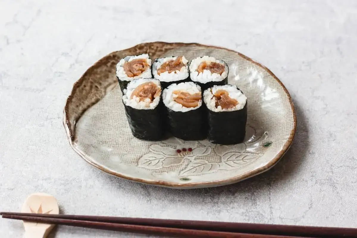 Sześć kawałków sushi z ryżem i nori, wypełnione delikatnym farszem z tykwy. Podane na ozdobnym talerzu z pałeczkami.