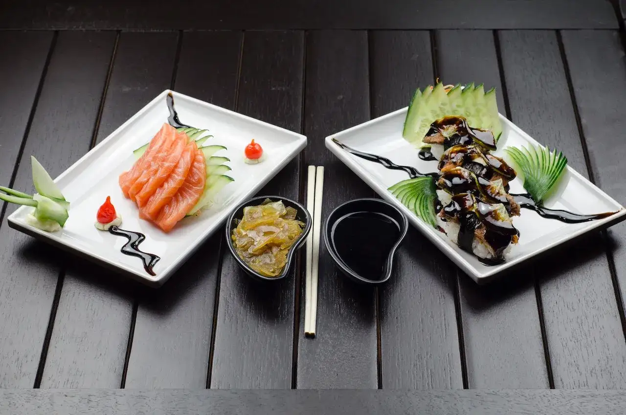 Dwa talerze z sushi, jedno z łososiem, drugie z węgorzem. Sushi, które pochodzi z Japonii, prezentuje się apetycznie.