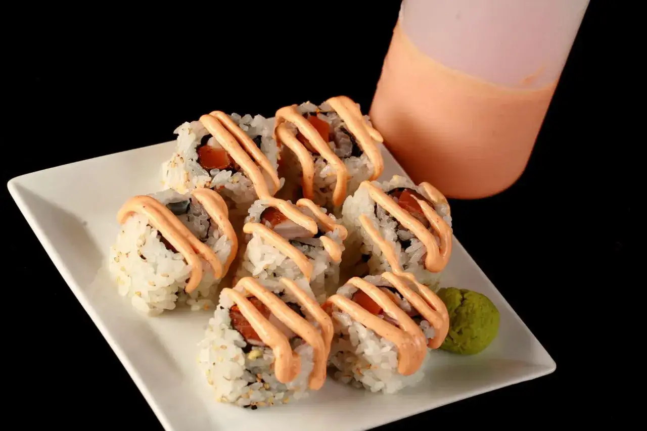 Sześć roladek sushi polanych kremowym, słodkim sosem do sushi. Obok porcja wasabi.
