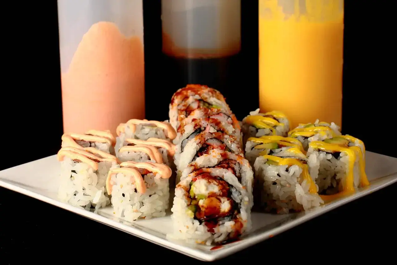 Talerz sushi z różnymi sosami, w tym słodki sos do sushi w butelce.