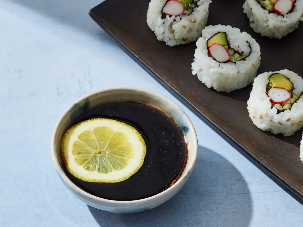 Sos do sushi przepis: aromatyczny sos sojowy z plasterkiem cytryny i gotowe rolki sushi z awokado i paluszkami krabowymi.