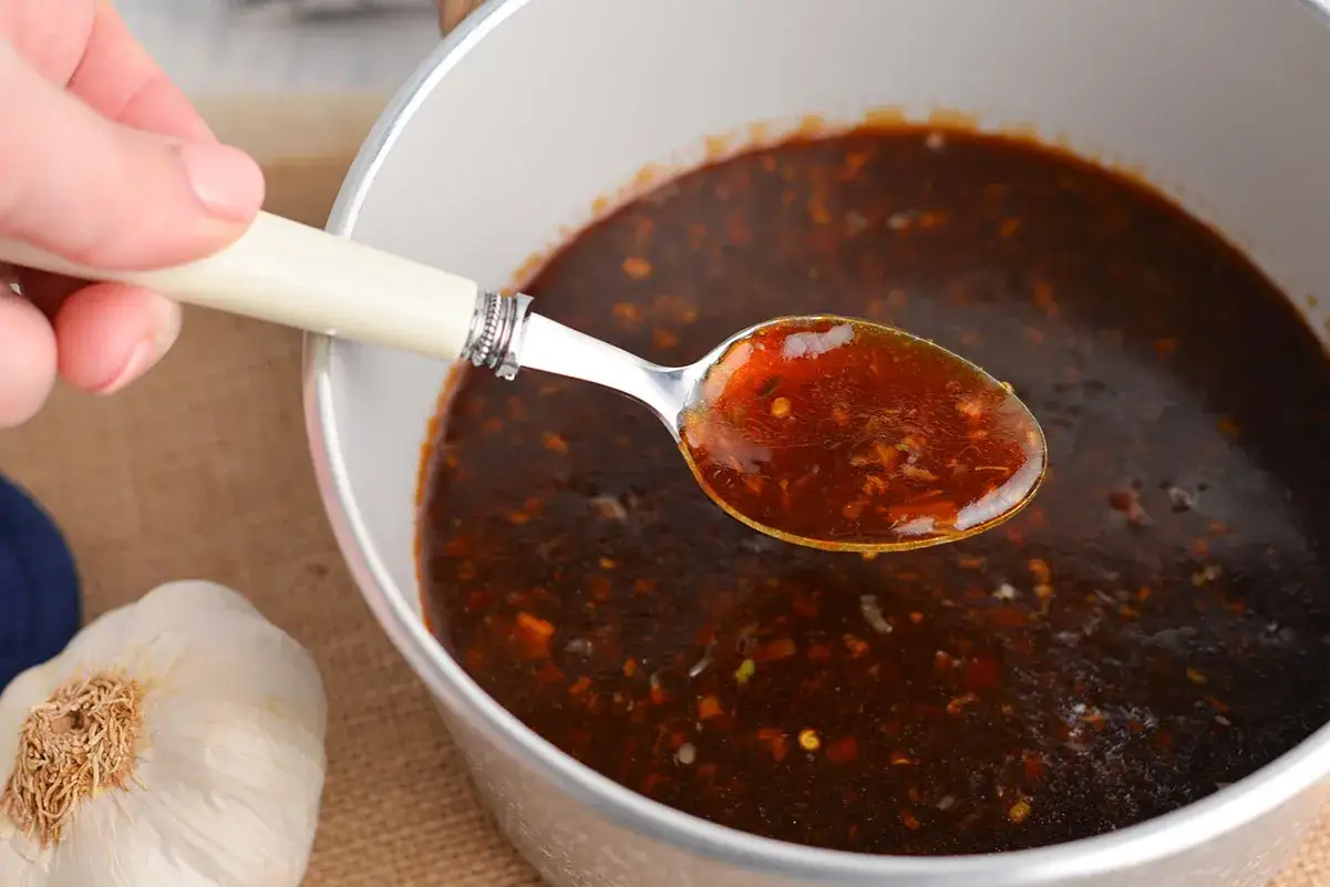 Łyżka z aromatycznym, ciemnym sosem chińskim do ryżu, obok główka czosnku.